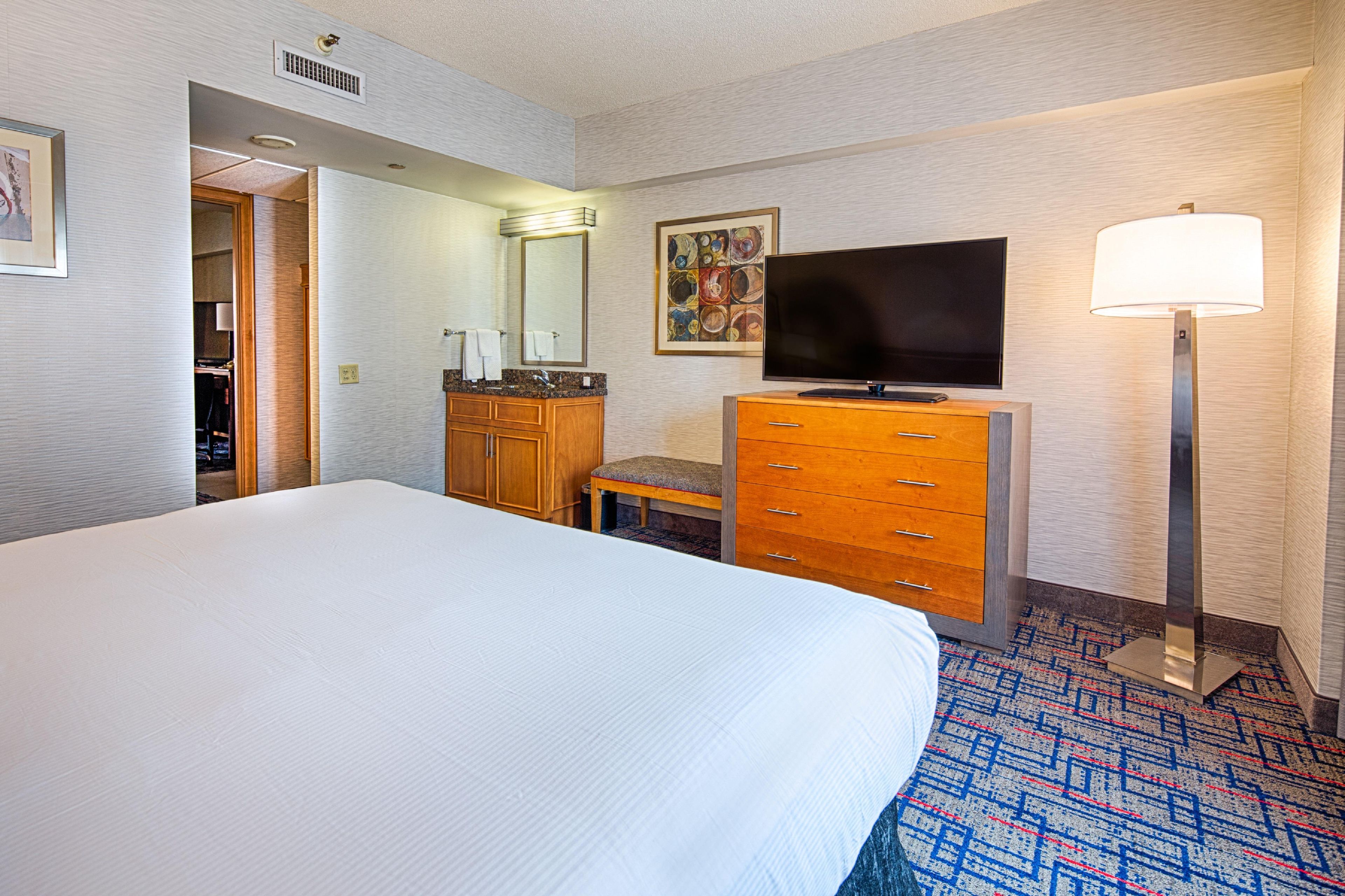 A hotel room with a large bed, a wooden dresser, a television, and a floor lamp.
