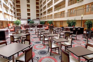 A hotel lobby with multiple dining areas, tables, and chairs.