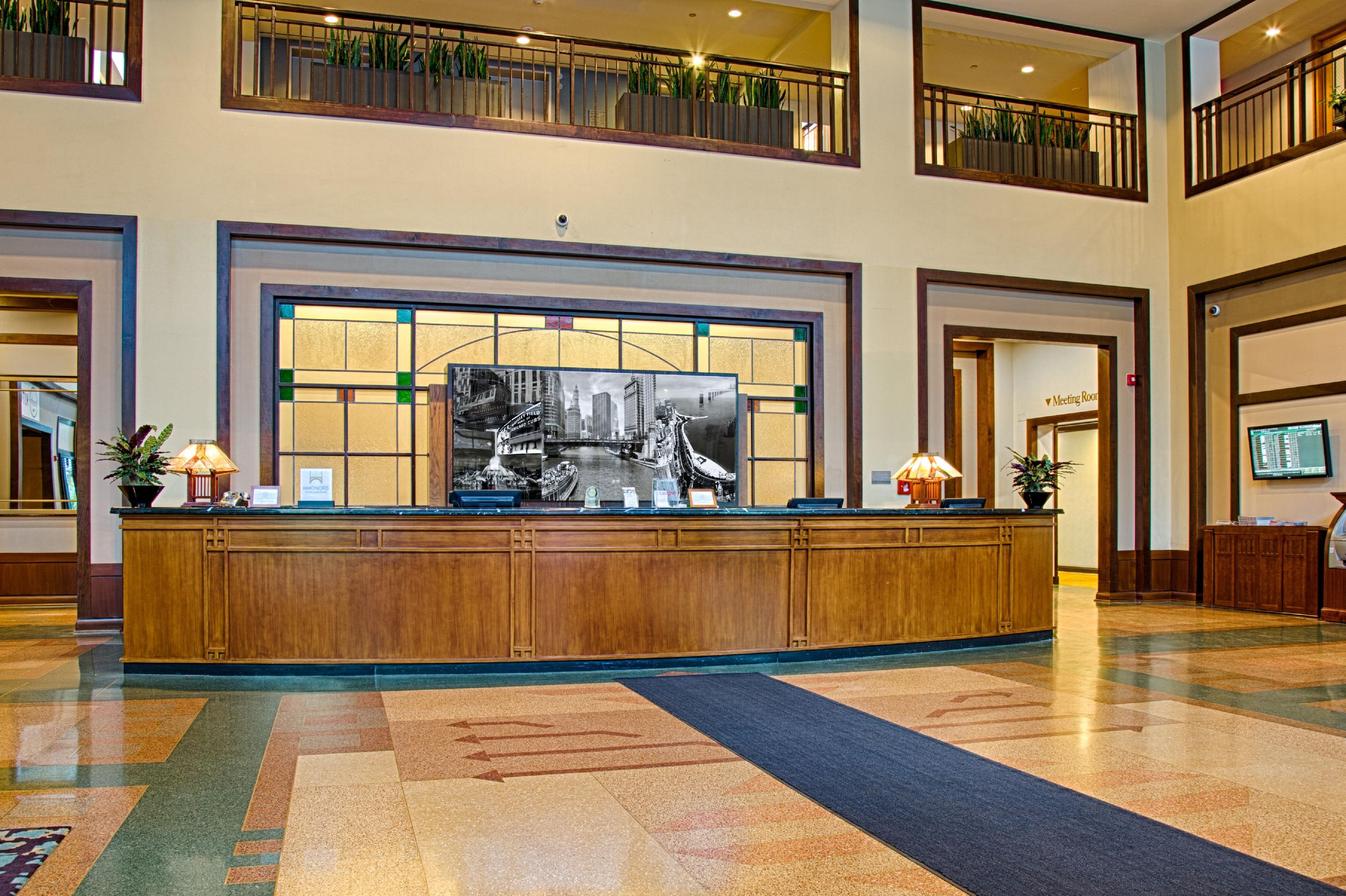 A hotel lobby with a reception desk, a large window with a view of a cityscape, and a meeting room door.