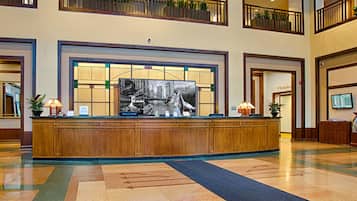 A hotel lobby with a reception desk, a large window with a view of a cityscape, and a meeting room door.