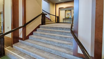 A carpeted staircase with a handrail, leading to a room with a desk and a plant.