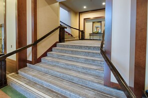 Eine Teppichstufenreife Treppe mit Handlauf, die zu einem Raum mit Schreibtisch und Pflanze führt.