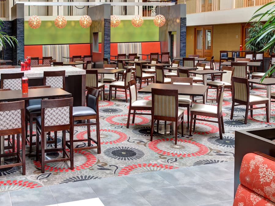 Un amplio comedor interior con varias mesas y sillas, una alfombra estampada y lámparas decorativas colgantes.