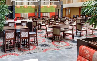 Un amplio comedor interior con varias mesas y sillas, una alfombra estampada y lámparas decorativas colgantes.