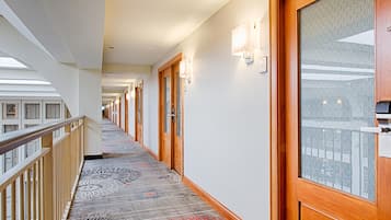 A hotel corridor with wooden doors, patterned carpet, and a railing on the left.
