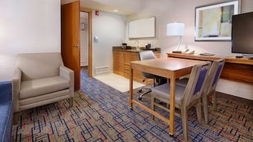 A hotel room with a dining table, two chairs, a TV, a desk, and a kitchen area.
