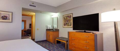 A hotel room with a large bed, a wooden dresser, a television, and a desk with a chair.