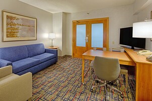 Habitación de hotel con un sofá azul, un escritorio de madera, un televisor y una alfombra estampada.