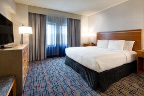A hotel room with a large bed, a TV, a desk, and a window with curtains. - Embassy Suites by Hilton Chicago O'Hare Rosemont (Rosemont)