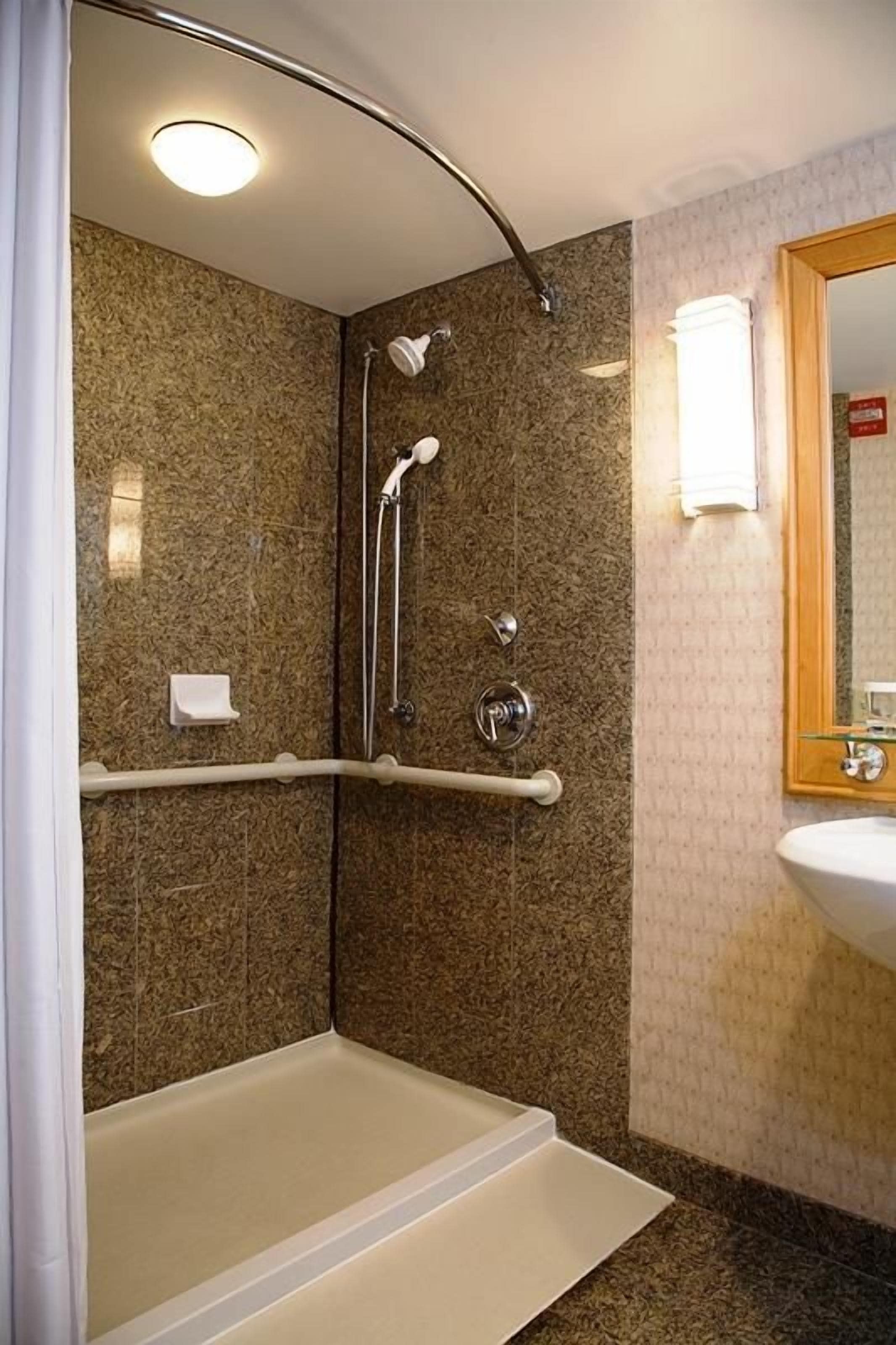 A bathroom with a walk-in shower, grab bar, and a sink with a mirror.