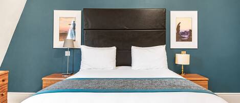 Ein Hotelzimmer mit einem großen Bett, einem dunklen Kopfteil, zwei Nachttischen mit Lampen und zwei gerahmten Bildern an den Wänden.