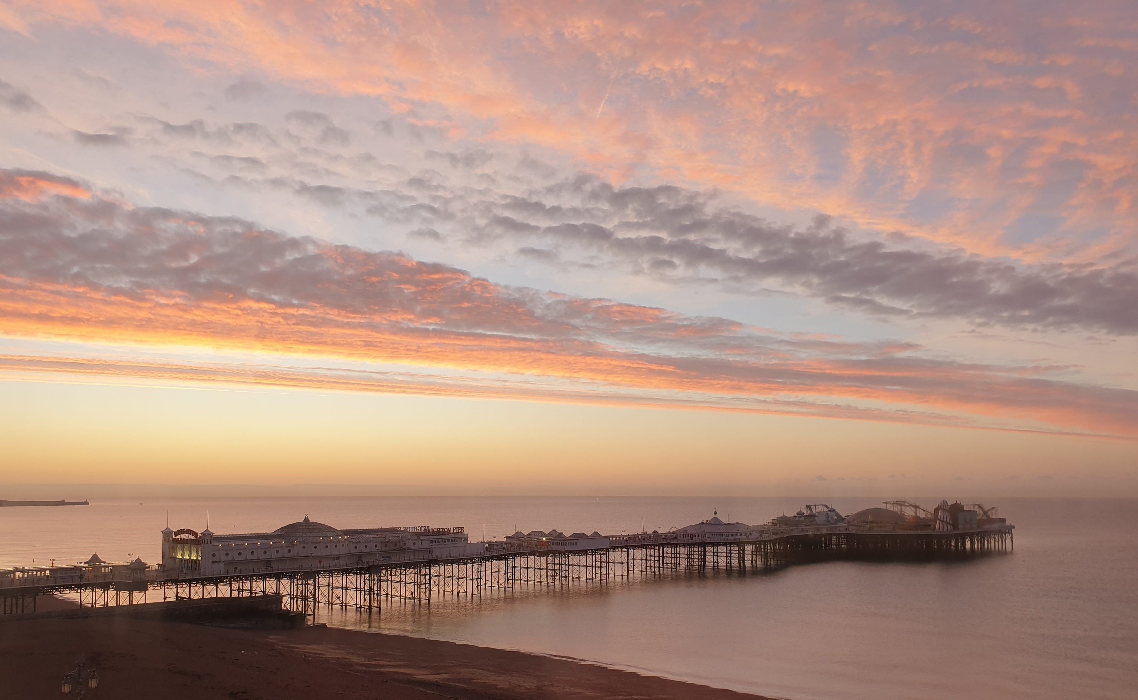 A pier extending into the water with buildings at the end, a clear sky, and a sunset.