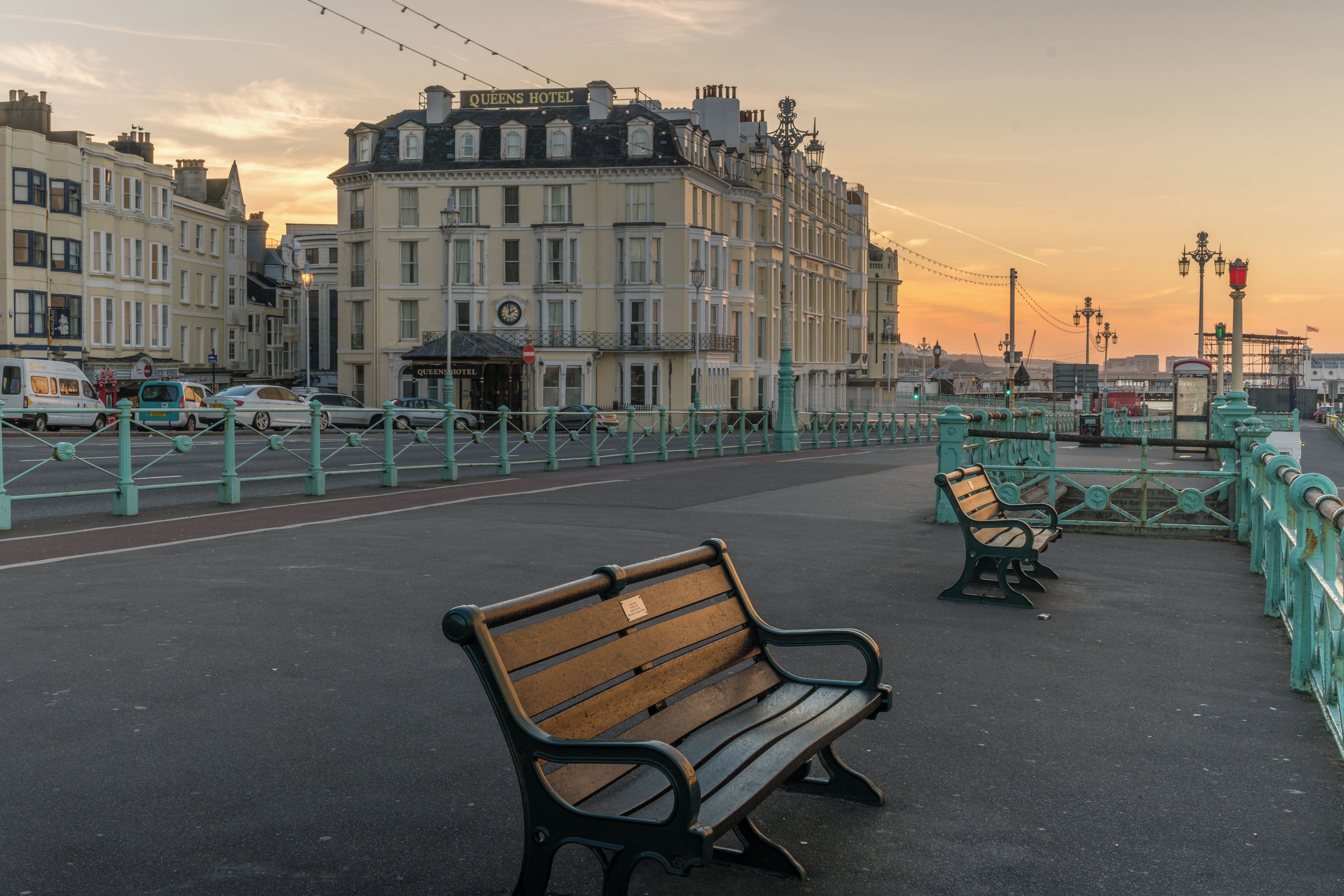 Eine Uferpromenade mit Bänken, dem Queens Hotel und klassischer Architektur.