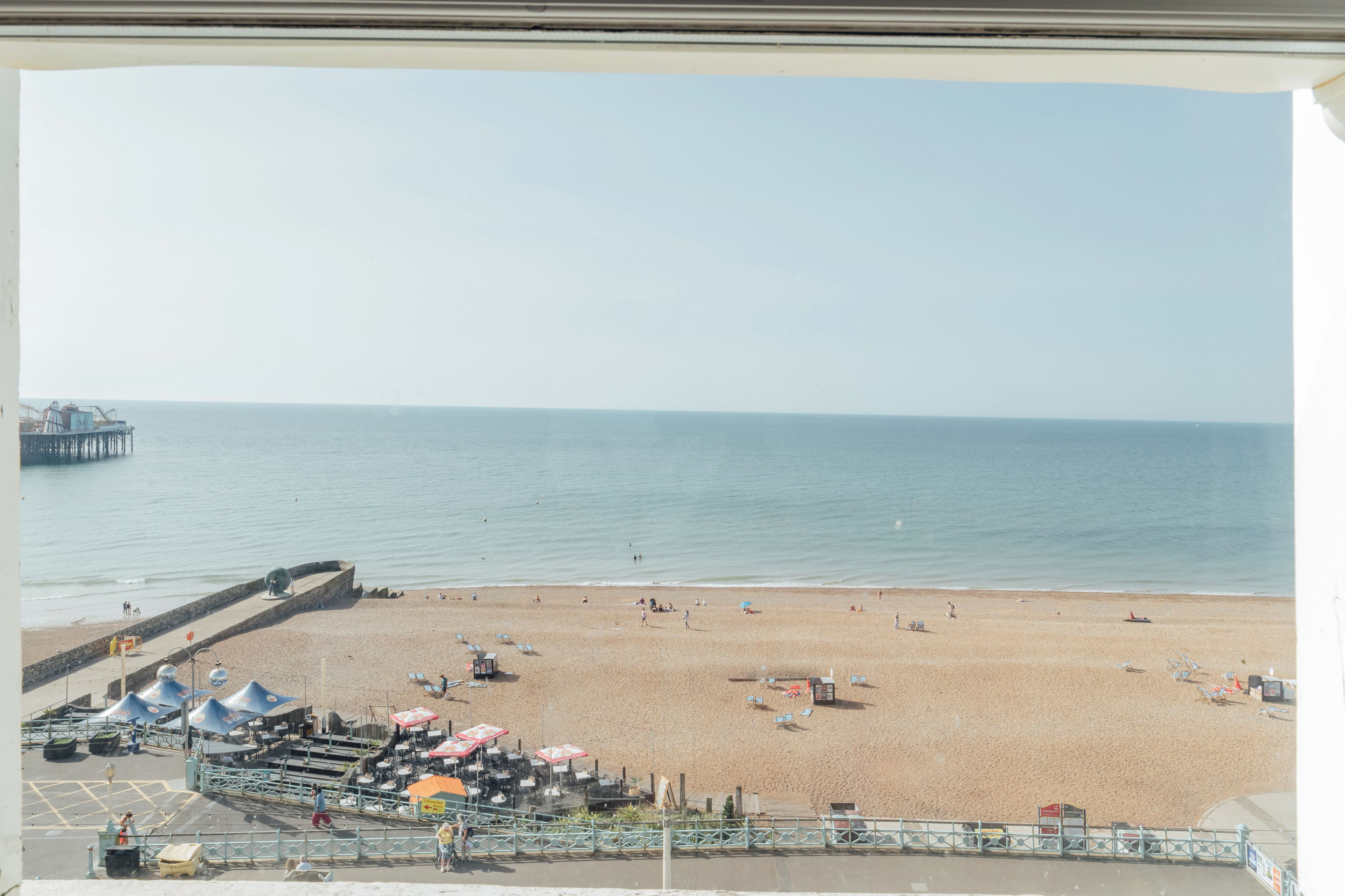 A beach with a pier in the background, umbrellas, and beach chairs.