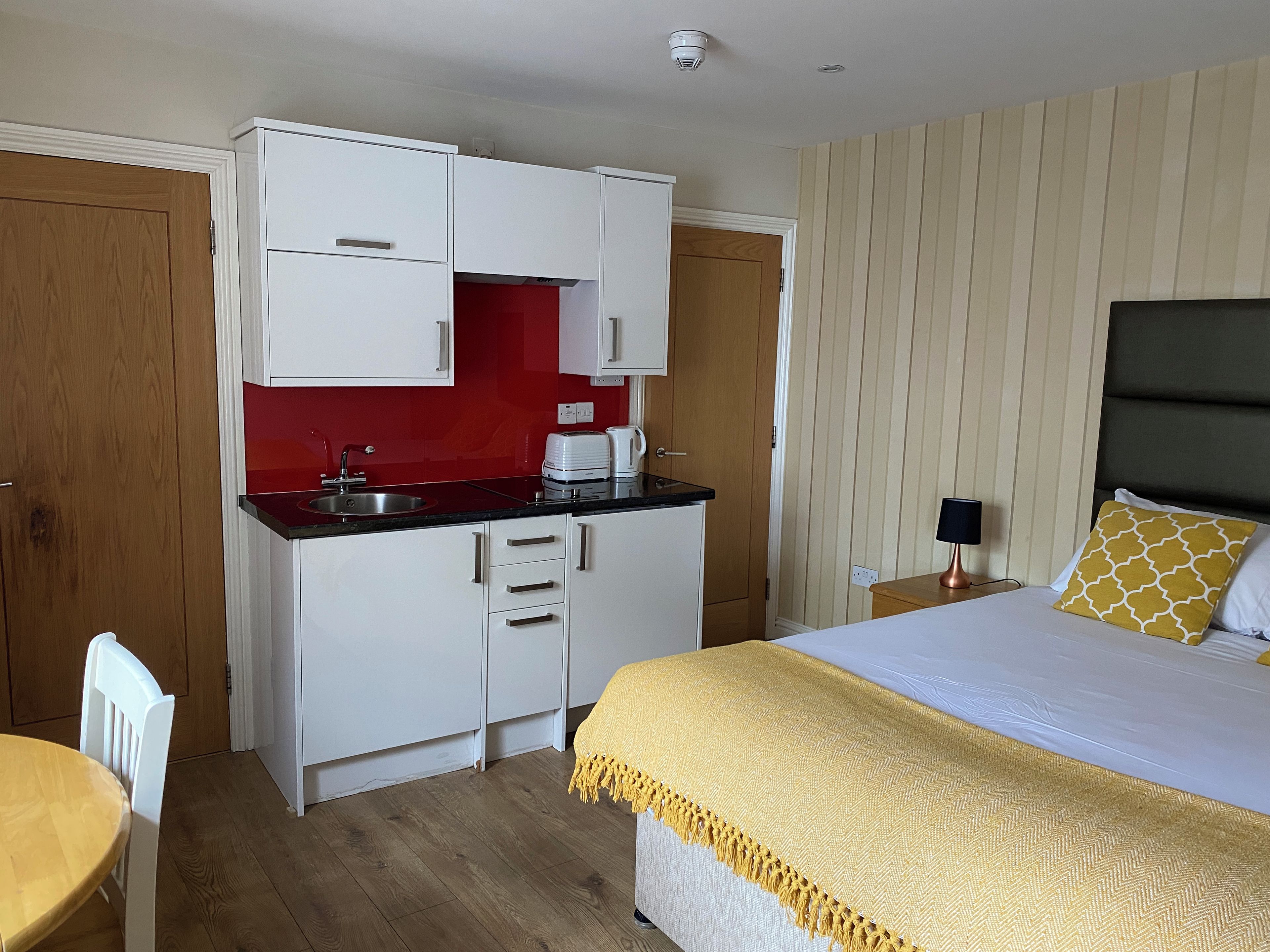 Une chambre d’hôtel compacte, dotée d’une kitchenette, d’un lit agrémenté d’oreillers à motifs et d’un plancher en bois.