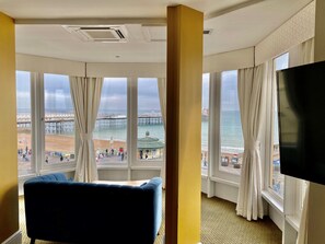 A hotel room with a large window offering a view of a pier and beach, a flat-screen TV, and a blue sofa.