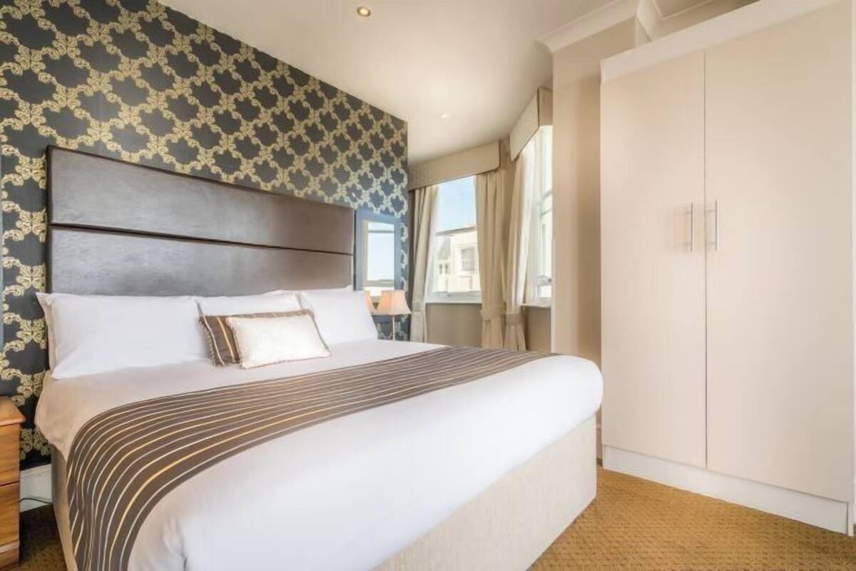 A hotel room with a large bed, a wardrobe, and patterned wallpaper.