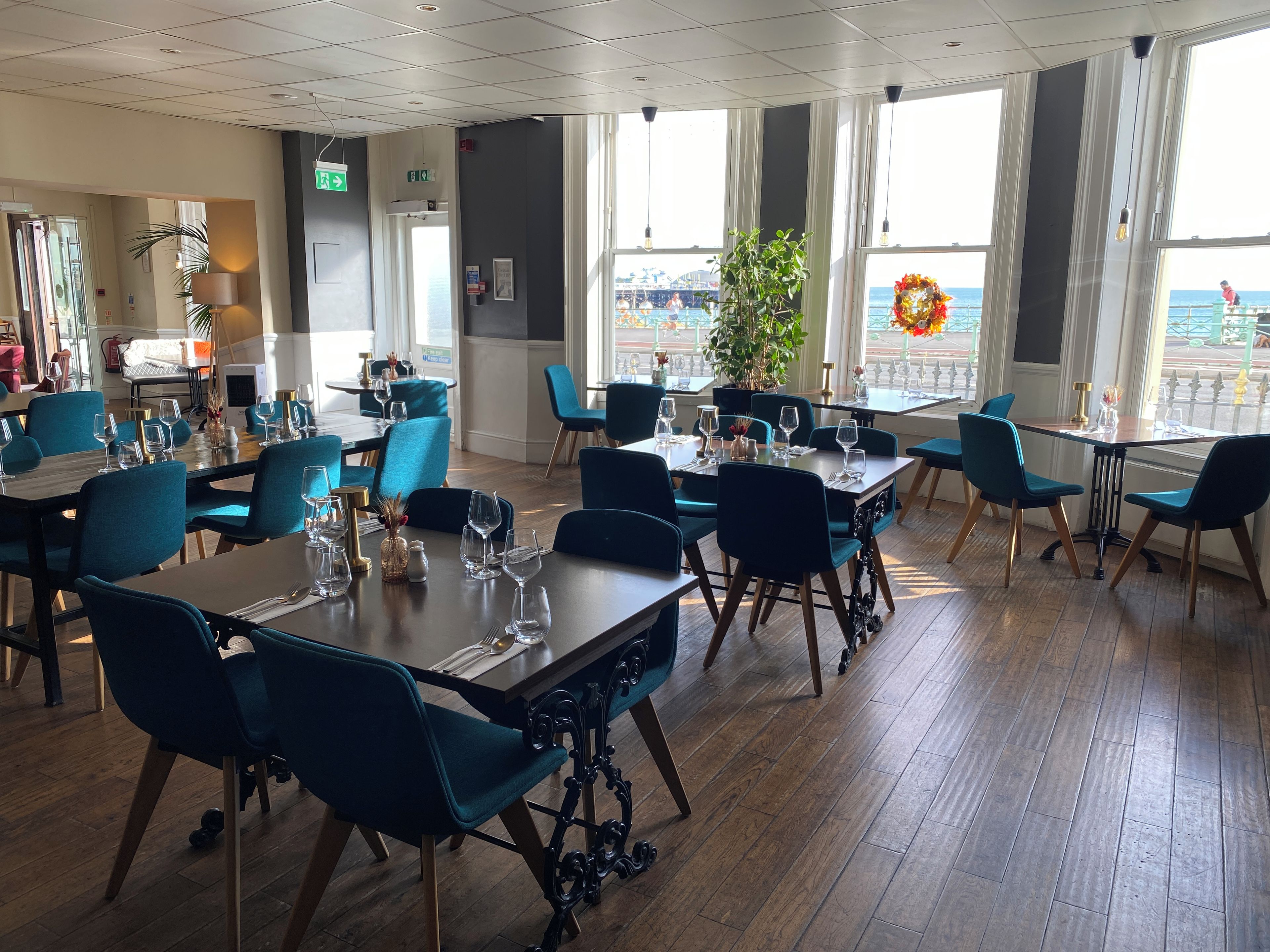 Un restaurant avec des tables dressées pour le service, des chaises et une vue sur la mer grâce à de grandes fenêtres.
