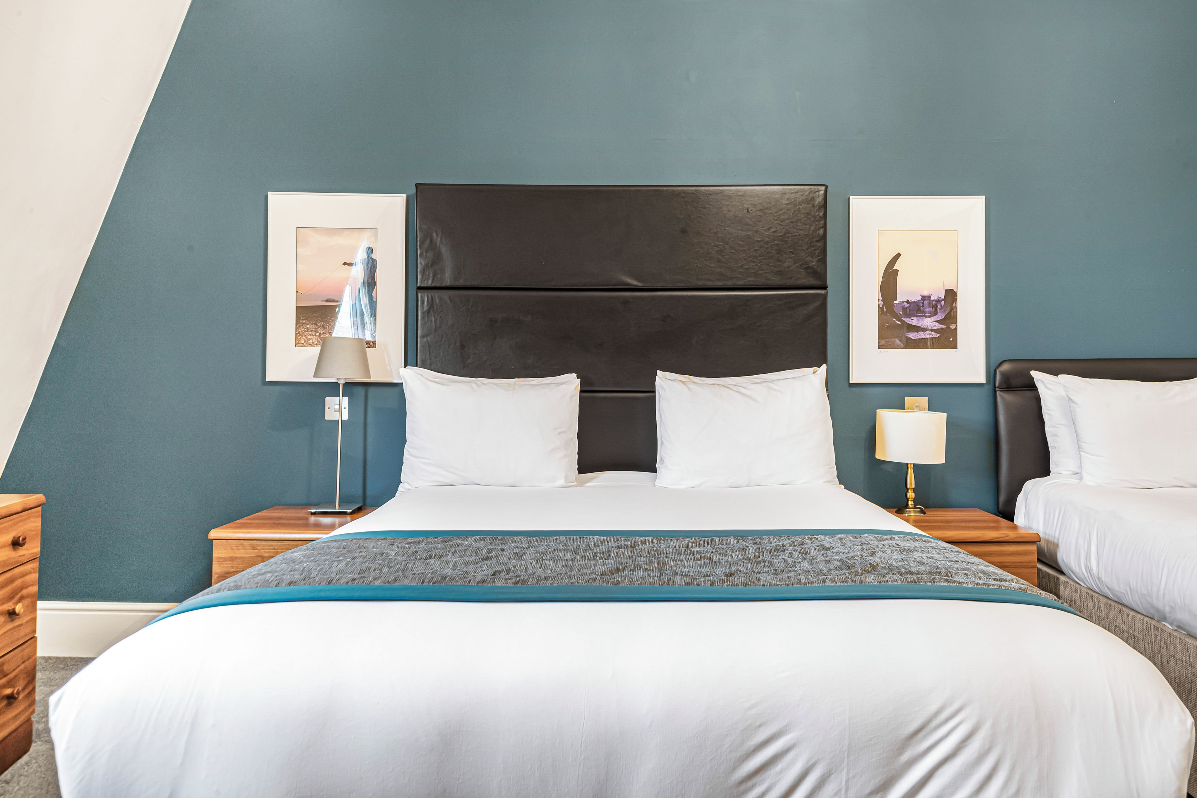 Habitación de hotel con una cama, dos mesitas de noche, una lámpara y dos cuadros en la pared.