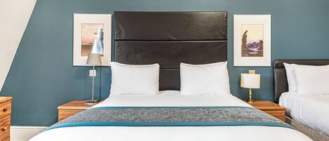 A hotel room with a bed, two bedside tables, a nightstand, a lamp, and two framed pictures on the wall.