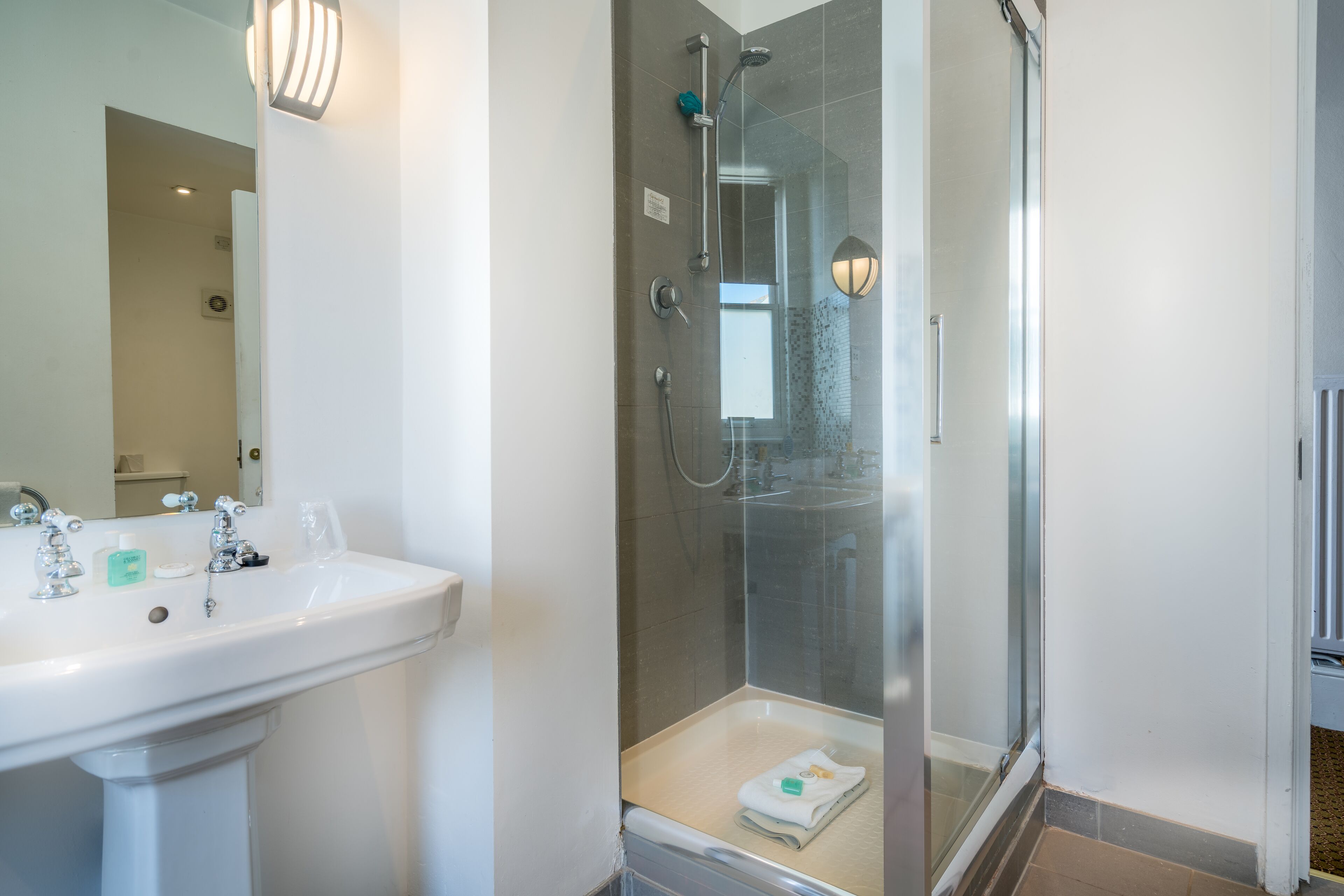 Een moderne badkamer met een witte wastafel, een douche met glazen wanden en een spiegel.