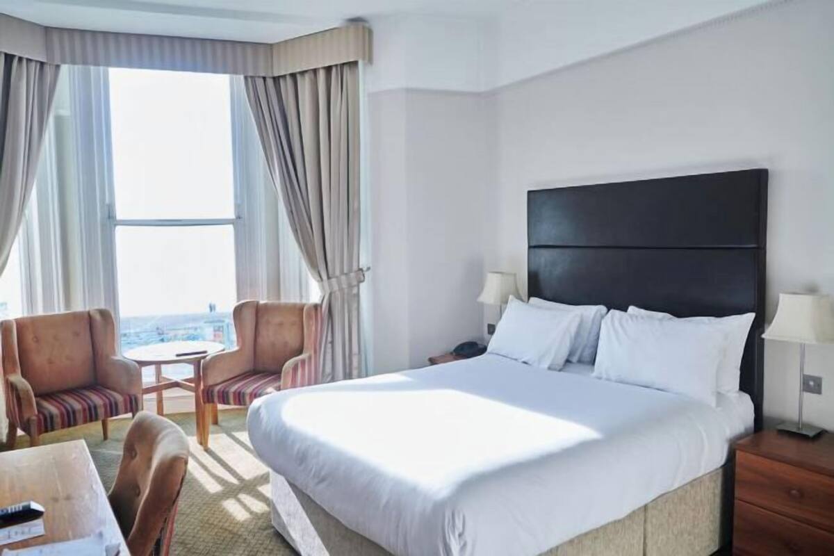 A hotel room with a large bed, a desk, two chairs, a small table, and a view of the city.