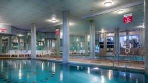 An indoor swimming pool with clear water, surrounded by glass walls and white lounge chairs. - Queens Hotel (Brighton)