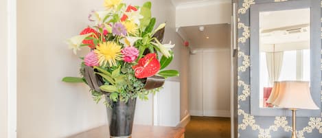 A wooden desk with a telephone, a vase of flowers, and a mirror on a wall.