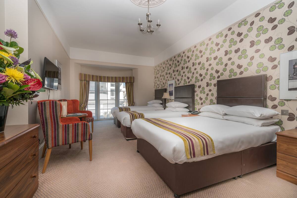 A hotel room with two single beds, a TV, a desk, a chair, and a large window with curtains.