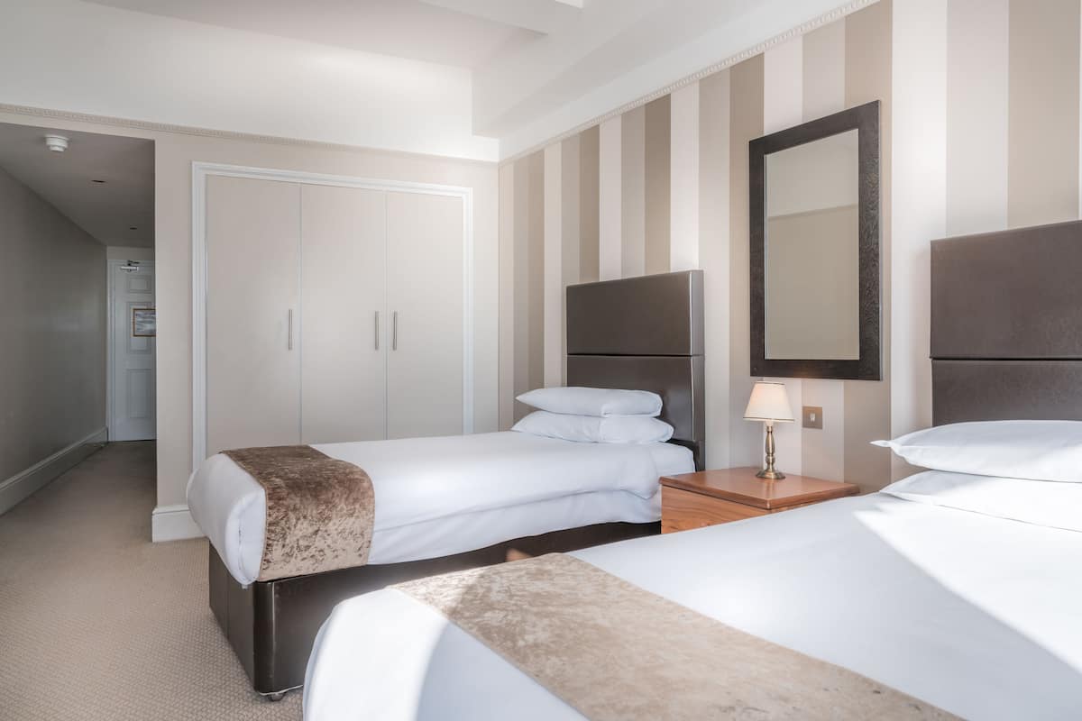 A hotel room with two beds, a wardrobe, a mirror, and a nightstand with a lamp.