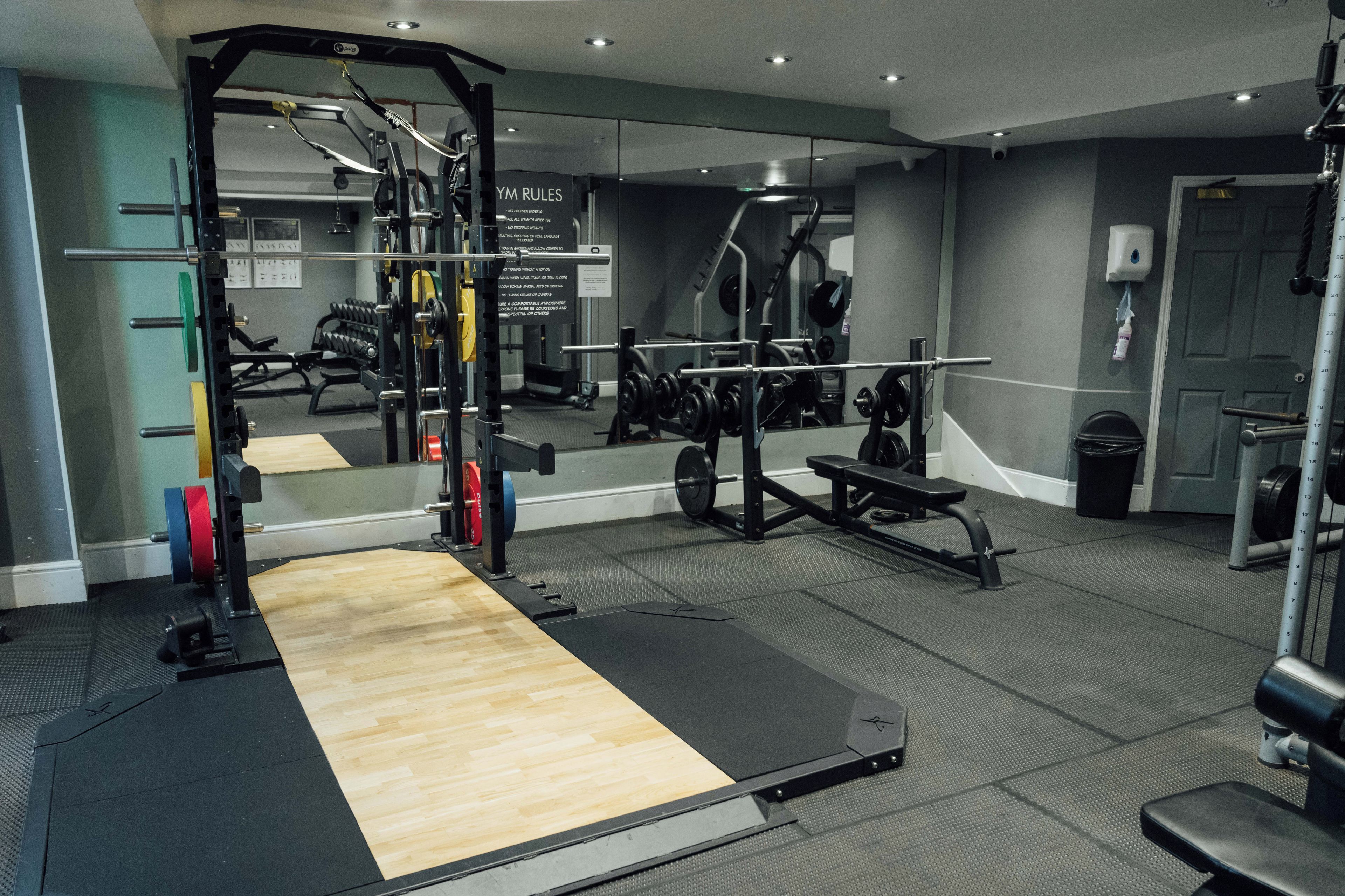 A gym with various exercise equipment, a mirror, and a wooden floor.