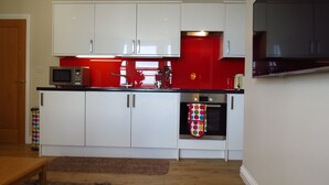 Una cocina moderna con gabinetes blancos, un salpicadero rojo y electrodomésticos de acero inoxidable.