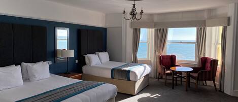 Habitación de hotel con dos camas, una mesa de comedor y vista al mar.
