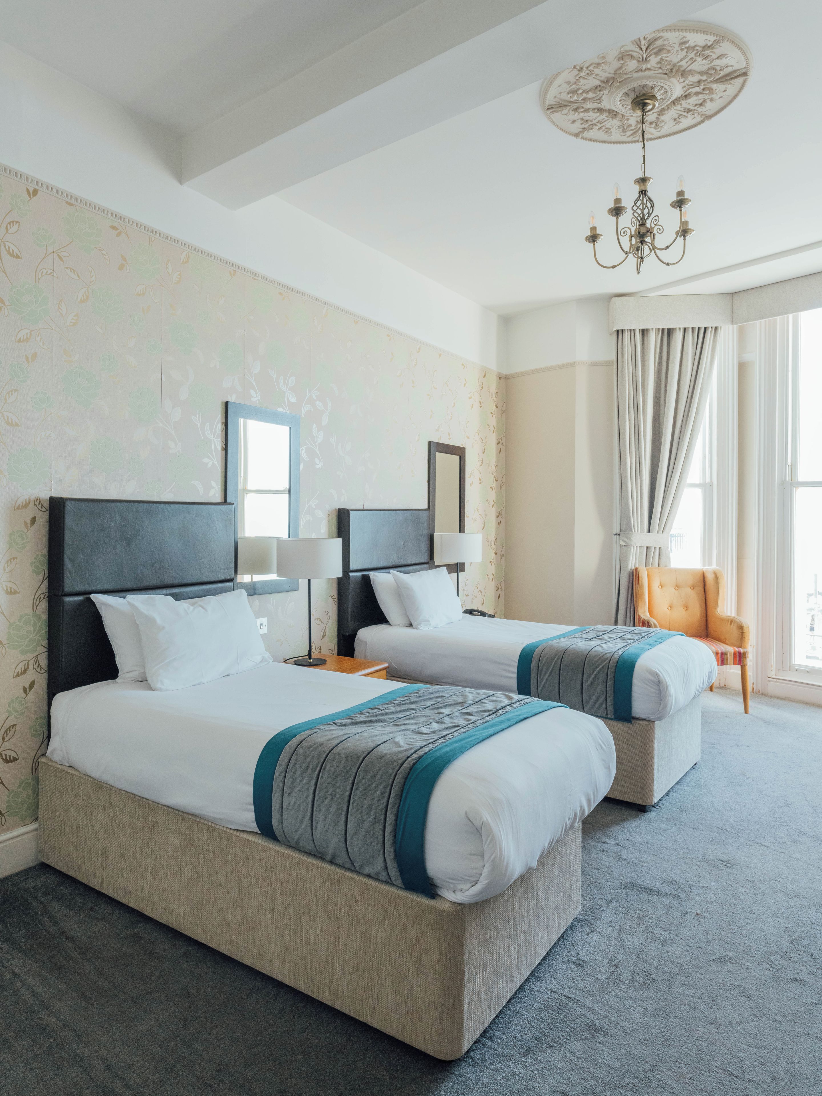 A hotel room with two beds, a chandelier, a chair, and a large window.