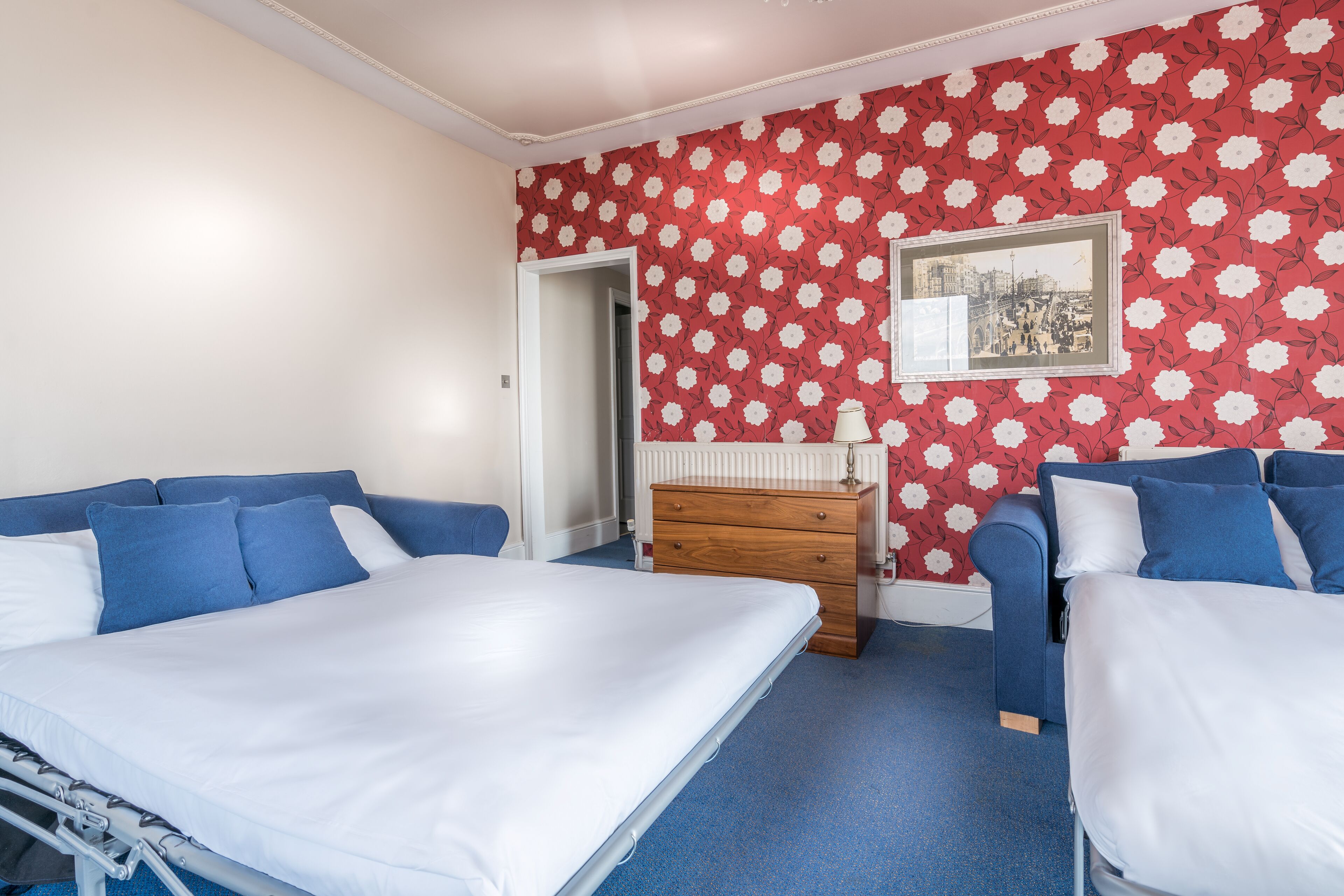 A hotel room with two beds, a wooden dresser, and a red floral wallpaper.