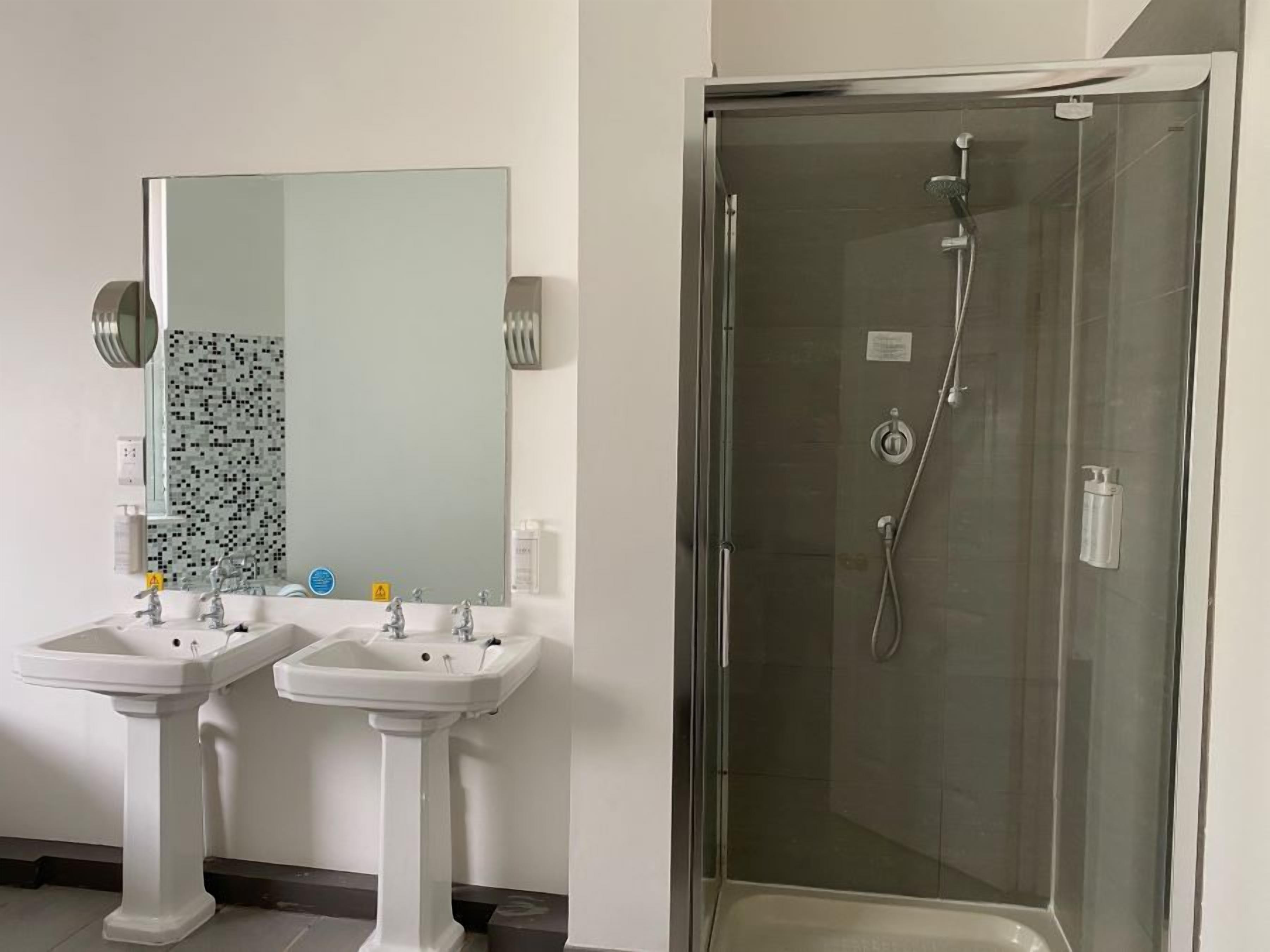 A bathroom with two pedestal sinks, a large mirror, and a glass-enclosed shower stall.