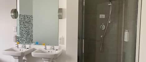 A bathroom with two pedestal sinks, a large mirror, and a glass-enclosed shower stall.