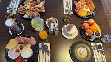 A breakfast table with various food items, drinks, and cutlery.