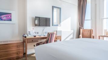 A hotel room with a large bed, a desk with a chair, a television, and a window with curtains.