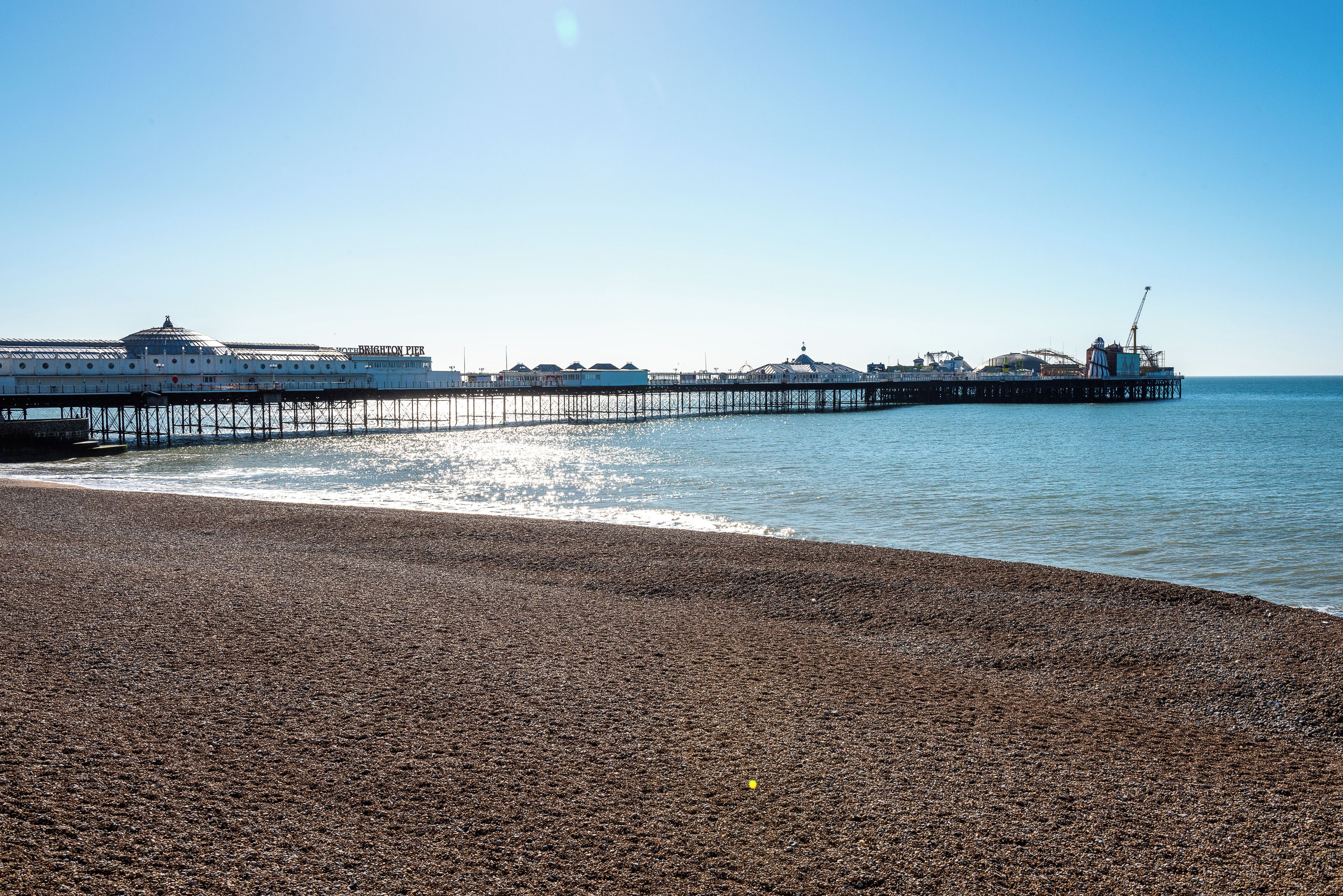 Una playa de guijarros con un muelle que se adentra en el mar, con un edificio de cúpula y el texto 'Brighton Pier'.