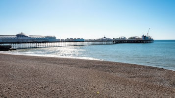 Una playa de guijarros con un muelle que se adentra en el mar, con un edificio de cúpula y el texto 'Brighton Pier'.