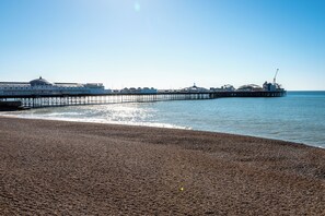 Una playa de guijarros con un muelle que se adentra en el mar, con un edificio de cúpula y el texto 'Brighton Pier'.
