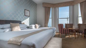 Habitación de hotel con una cama grande, una mesita, una silla y vistas al mar a través de las ventanas.