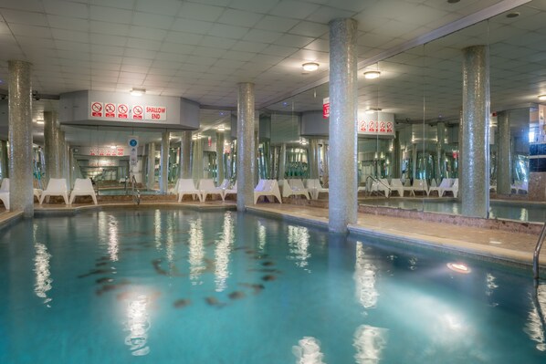 Una piscina interior con señalización clara, incluyendo una advertencia sobre la zona poco profunda.