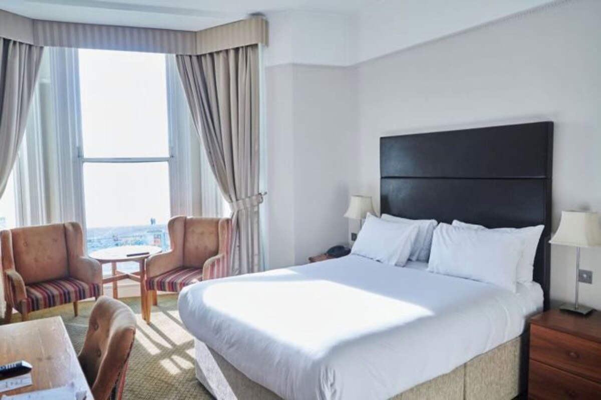 A hotel room with a large bed, a desk, two chairs, a small table, and a view of the city.