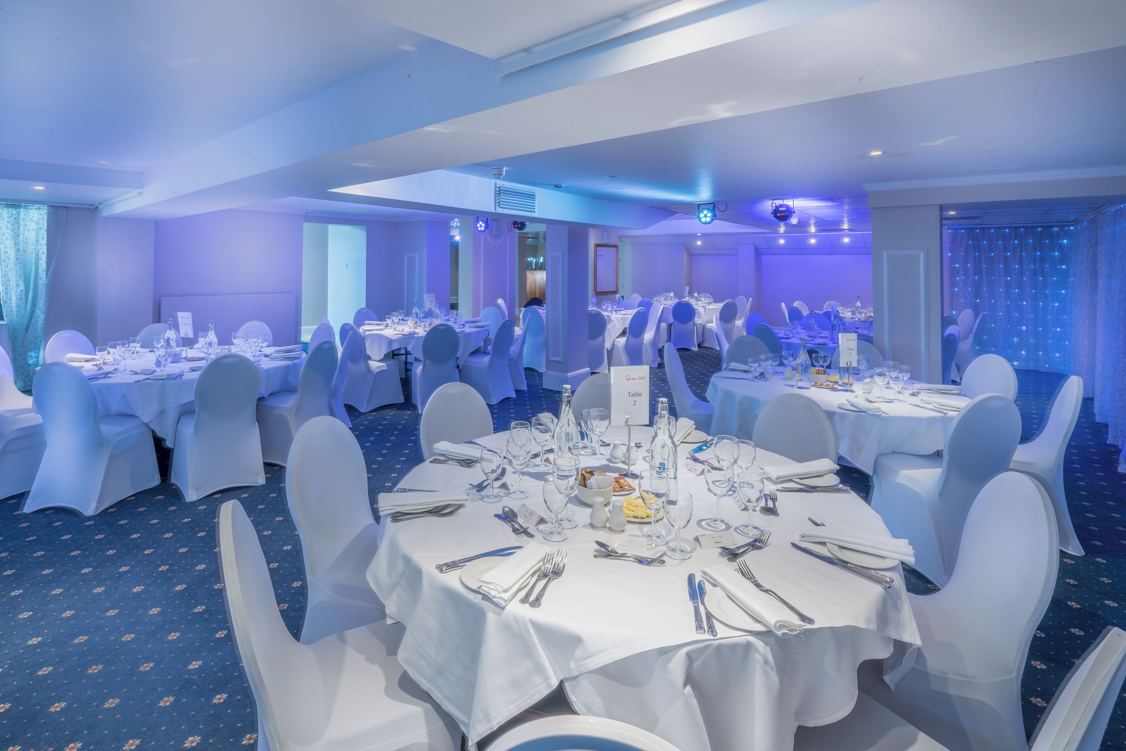 A banquet hall with round tables, white tablecloths, and chairs.