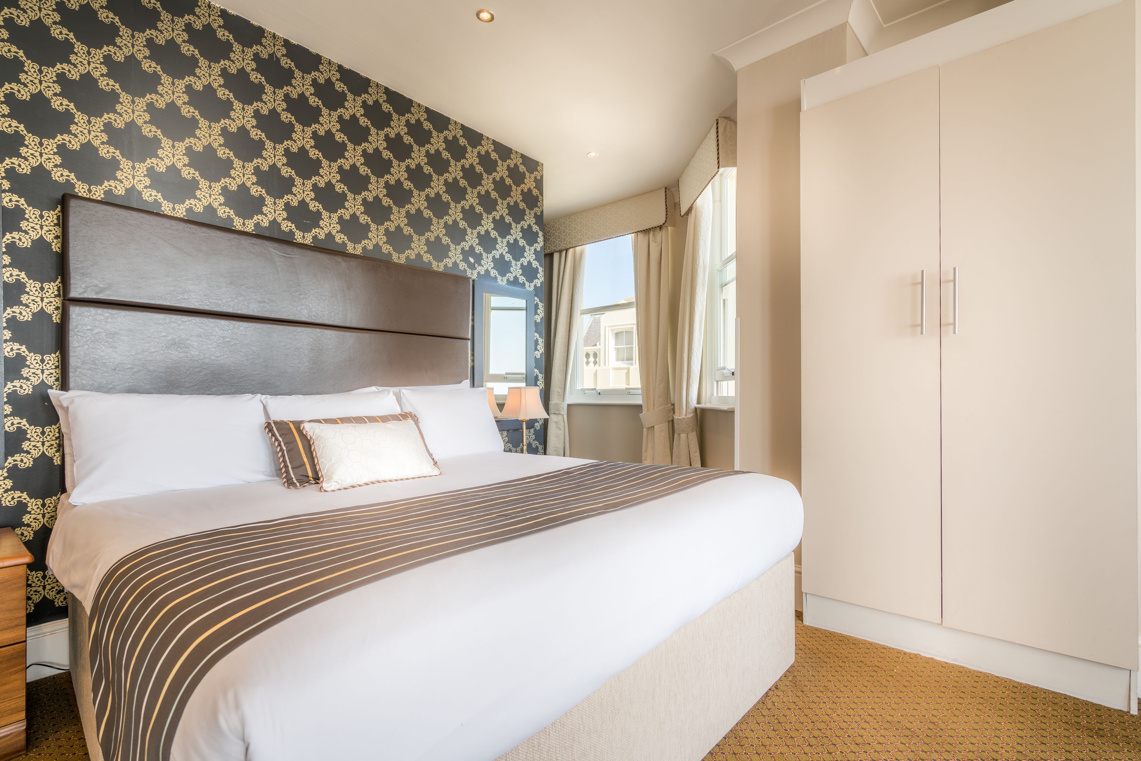 Una habitación de hotel con una cama grande, un armario y una ventana con cortinas.