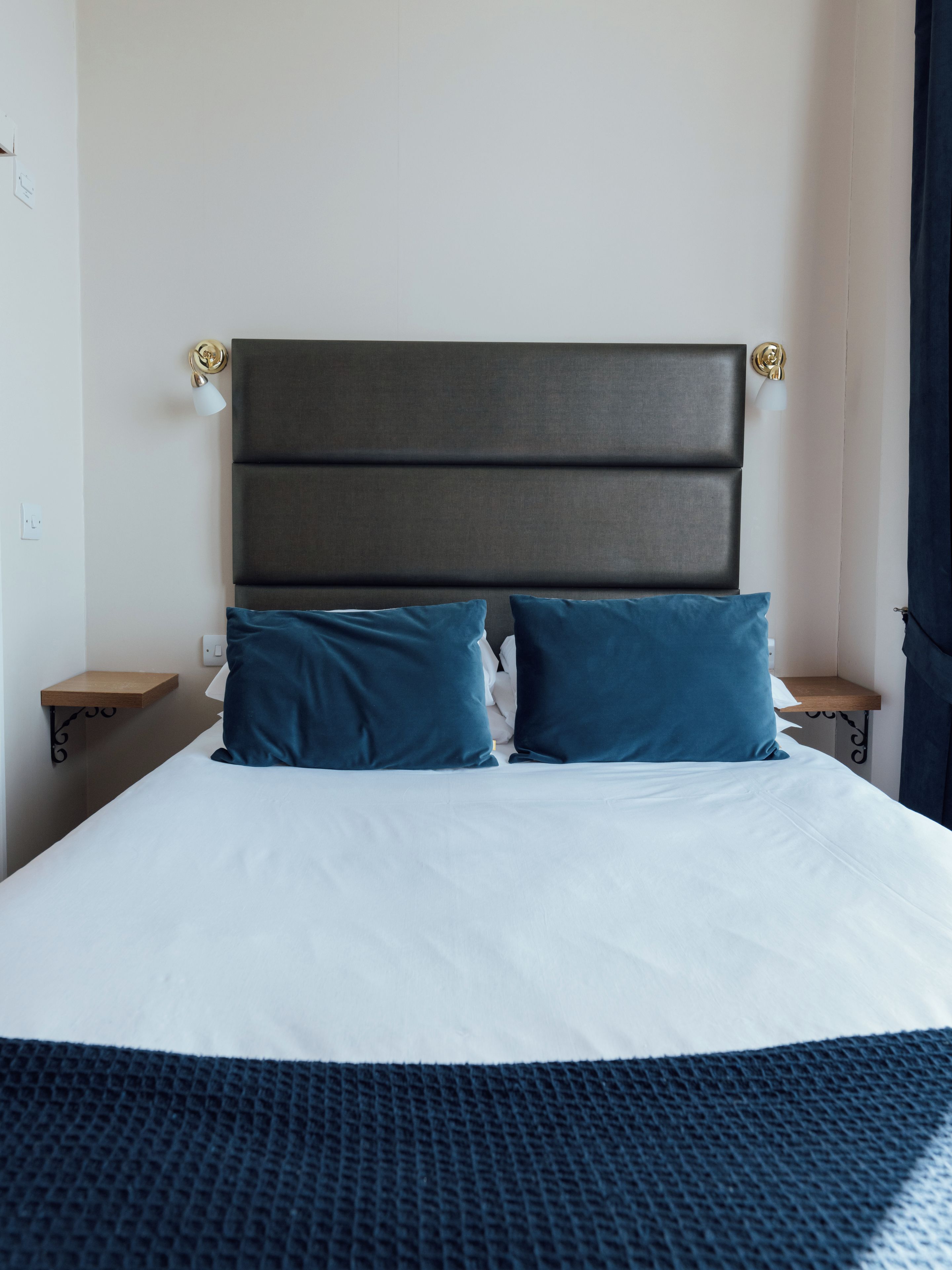 Una habitación de hotel con una cama grande, dos mesitas de noche y un cabecero con una lámpara.