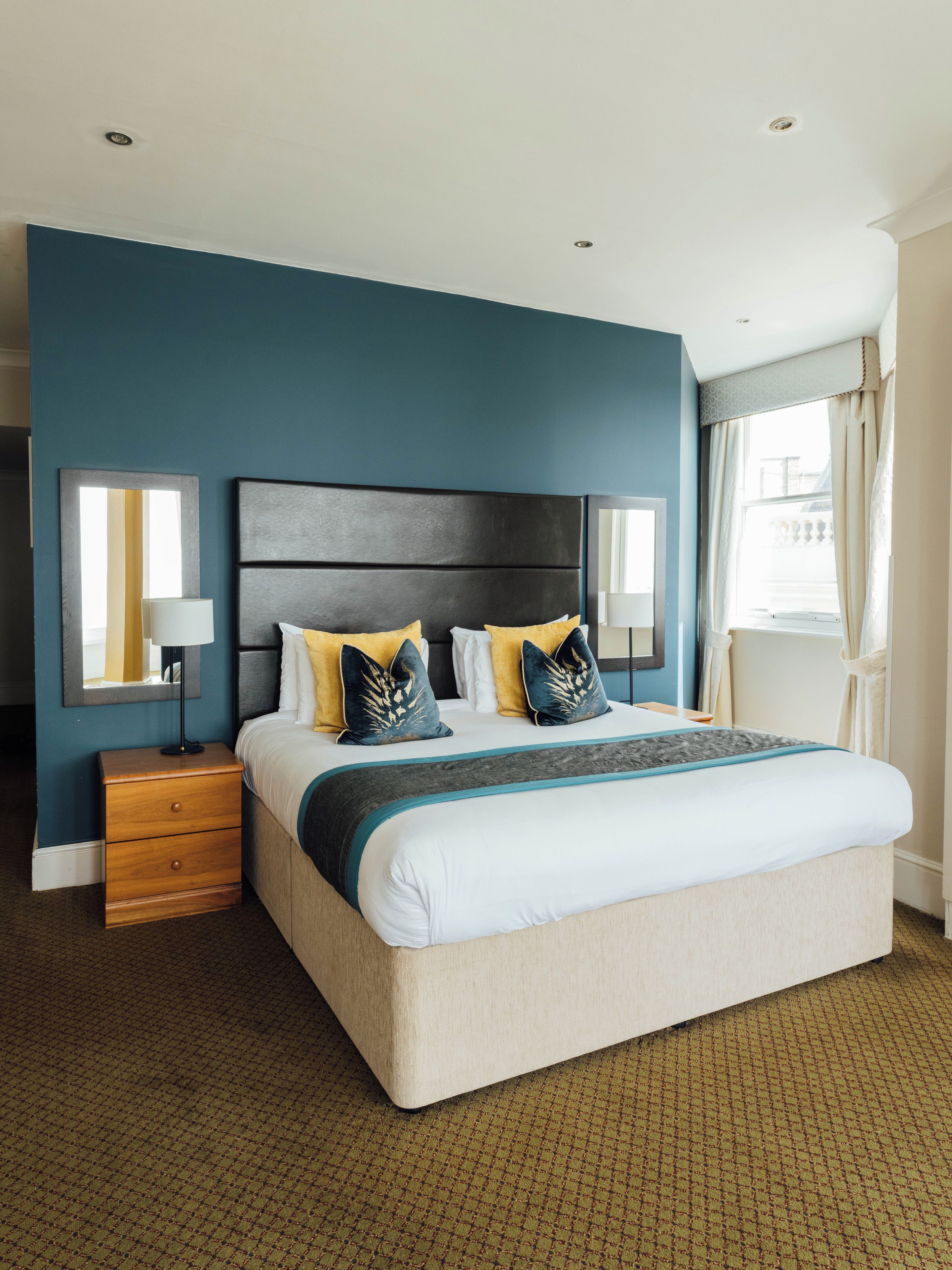 A hotel room with a large bed, a nightstand, a lamp, and a window with curtains.