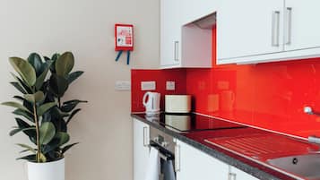 A modern kitchen with white cabinets, a red backsplash, and a wooden floor.